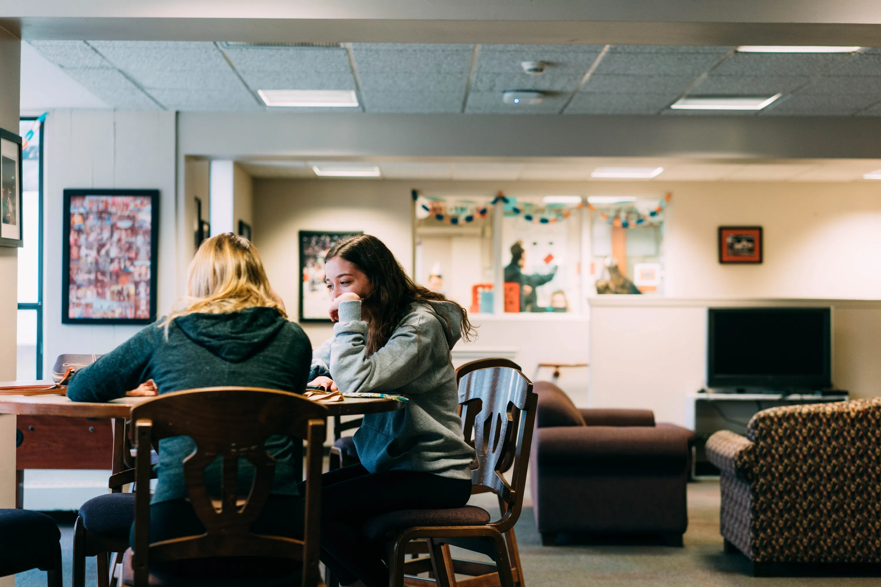 Two students sit together at a table in a cozy res hall lounge.