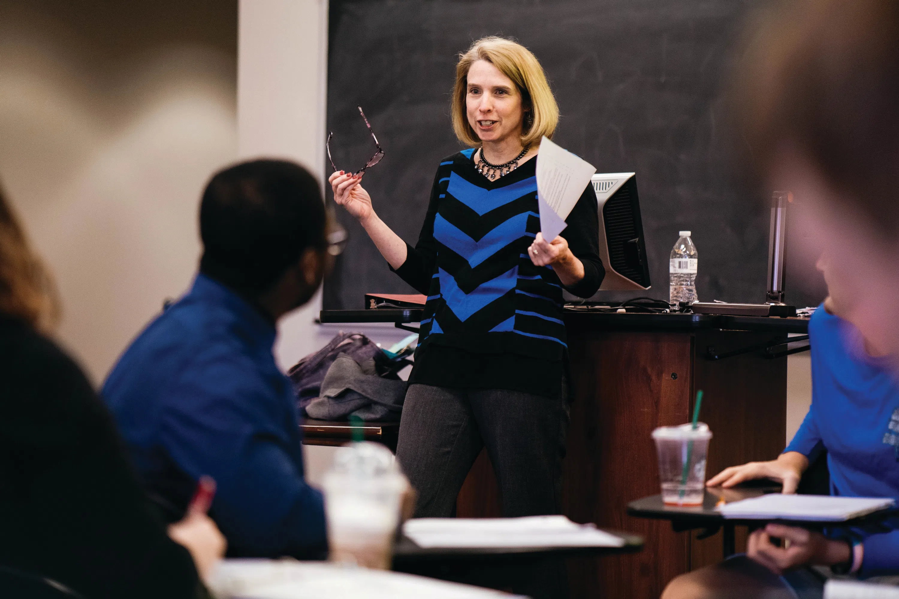 A faculty member stands among students during a classroom discussion.