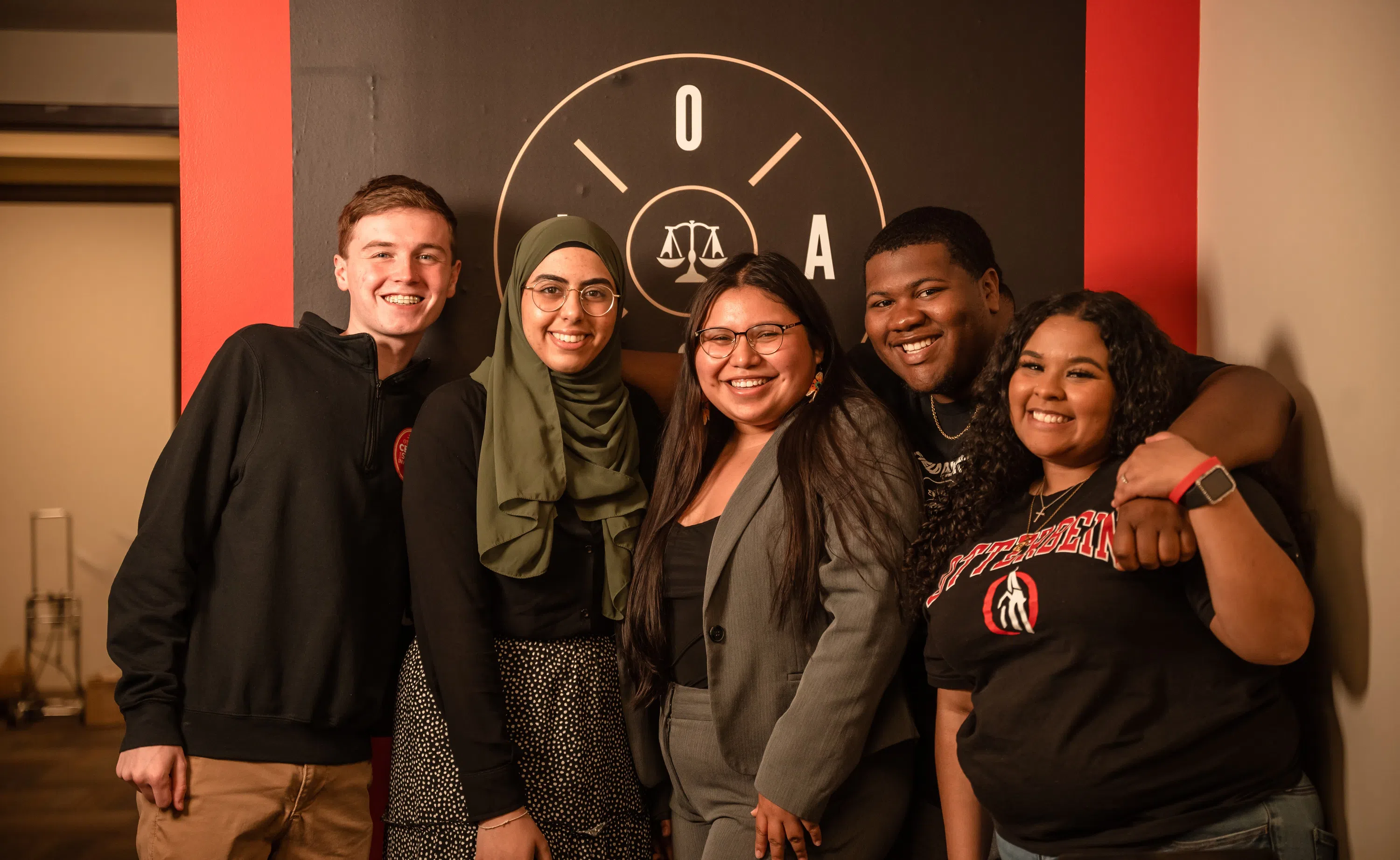 A group of students pose infront of the OSJA logo