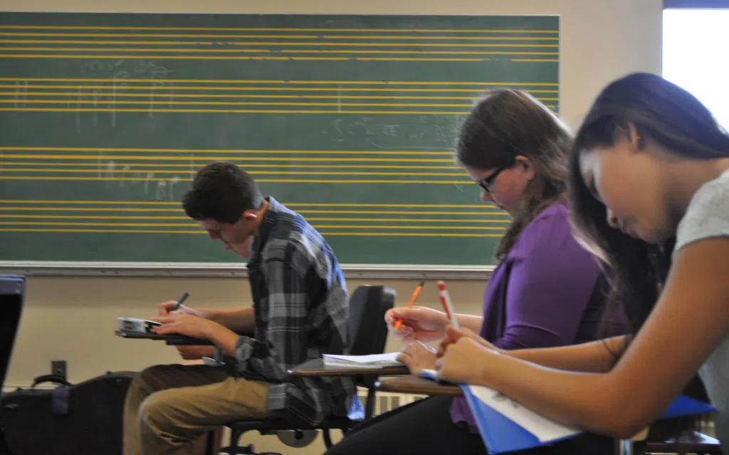 Students in a music class. There is a blackboard behind them with musical score.