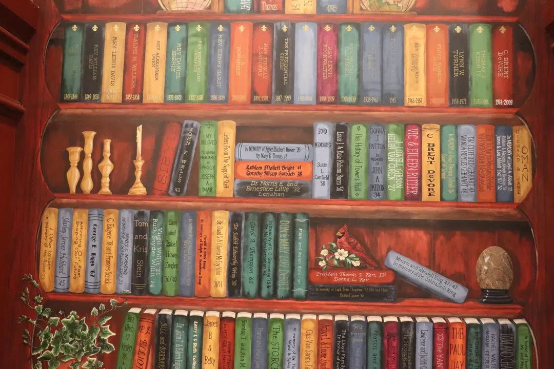 A painted bookshelf with hand painted books. These books have the names of various donors on the spine.