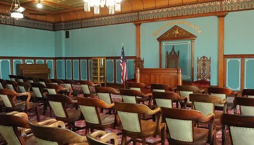 Room with green walls and medium wood accents. There are green cushioned chairs with the same medium wood accents facing a podium area