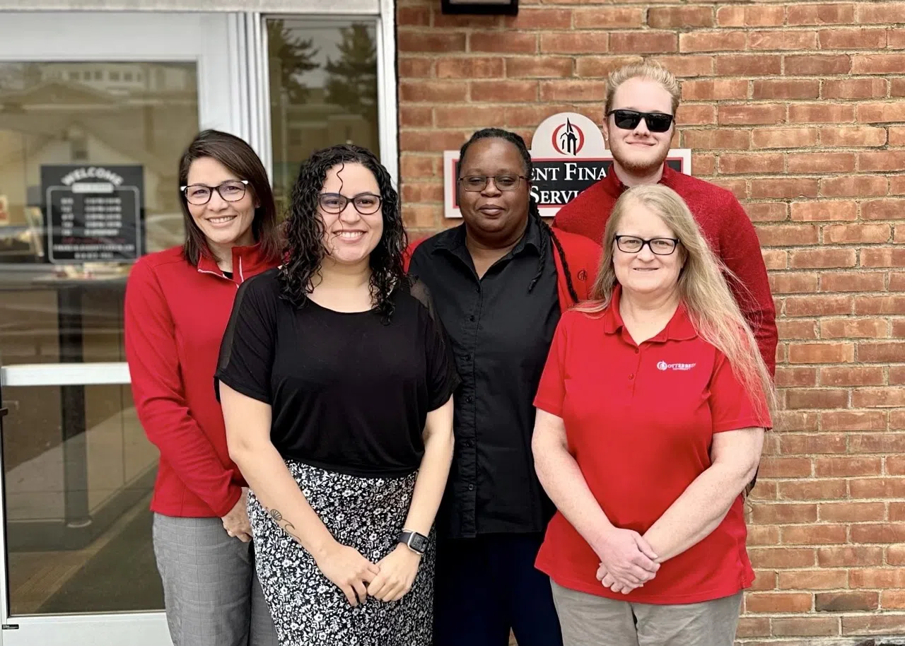 A group photo of the Financial Aid team. They are all smiling for the camera wearing black, red, and tan.