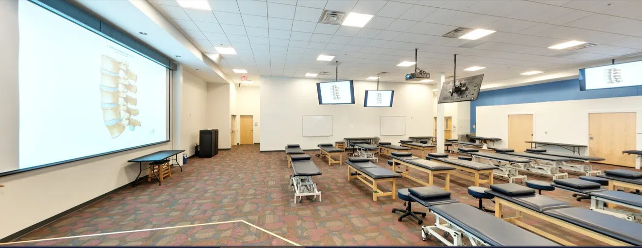 The OMM lab features benches for students to practice manipulations on each other. The room also features overhead projectors for viewing the demonstration being performed at the front of the classroom.