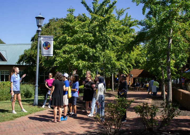 Student Ambassador is giving a tour to prospective students and family members  in front of the Library and Campus Center.