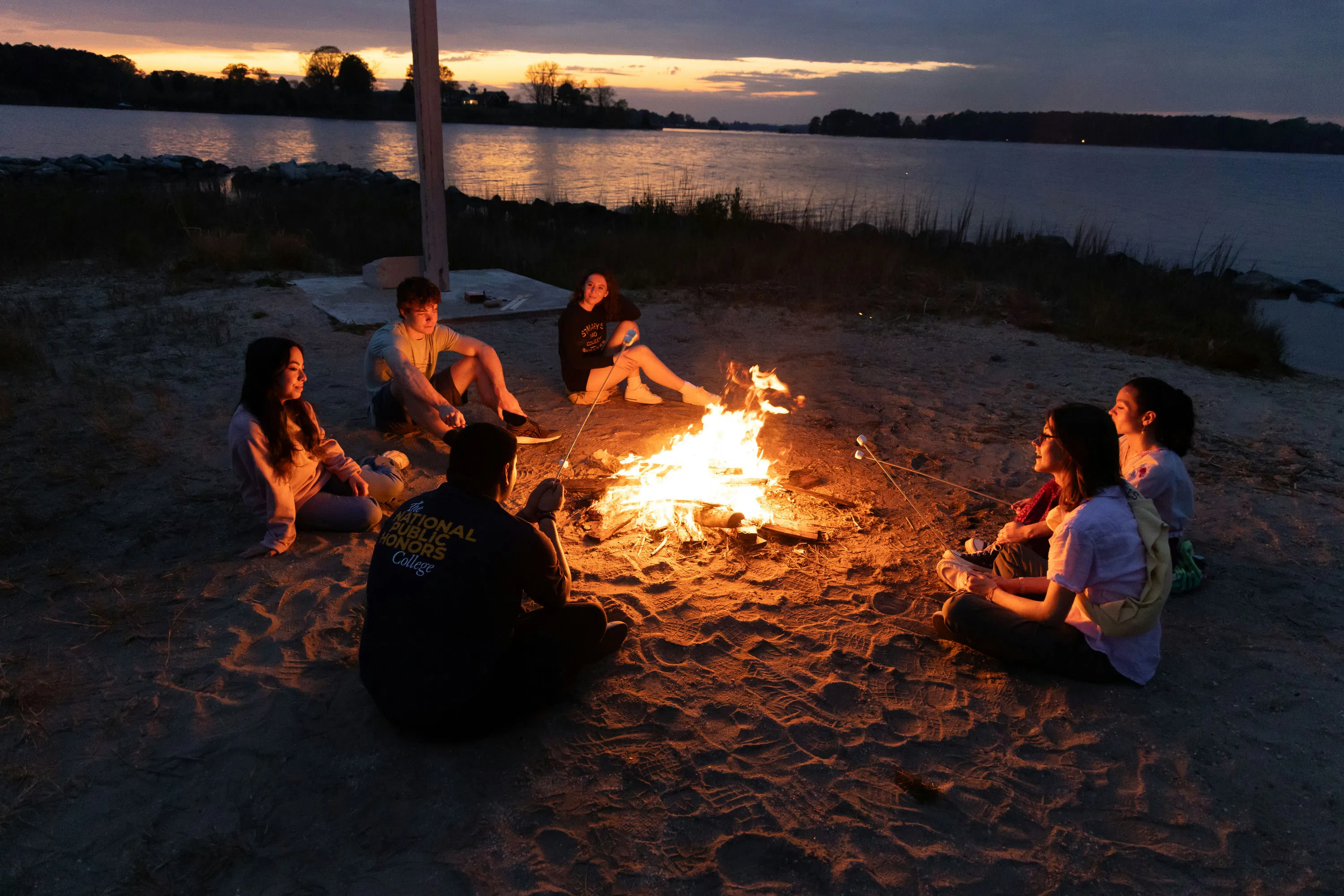 Students seated on the ground around a bonfire at church point at dusk.