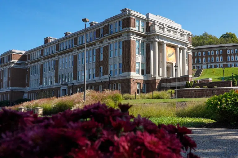 The image shows the exterior of Oglebay Hall, a long brick building with columns at the entrance.