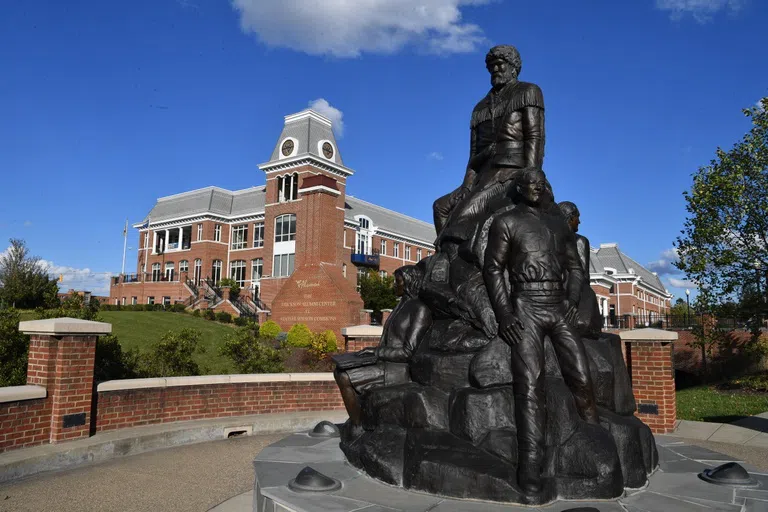 Image shows the exterior of Erickson Alumni Center, a red brick building with clock tower and mountaineer statue in the forefront. 