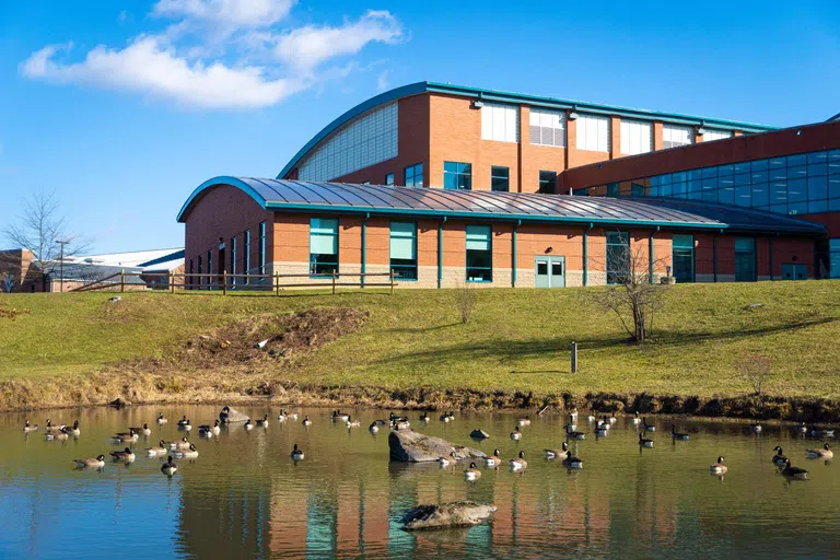 Exterior shot of building with a green curved roof and a scenic pond out front. 