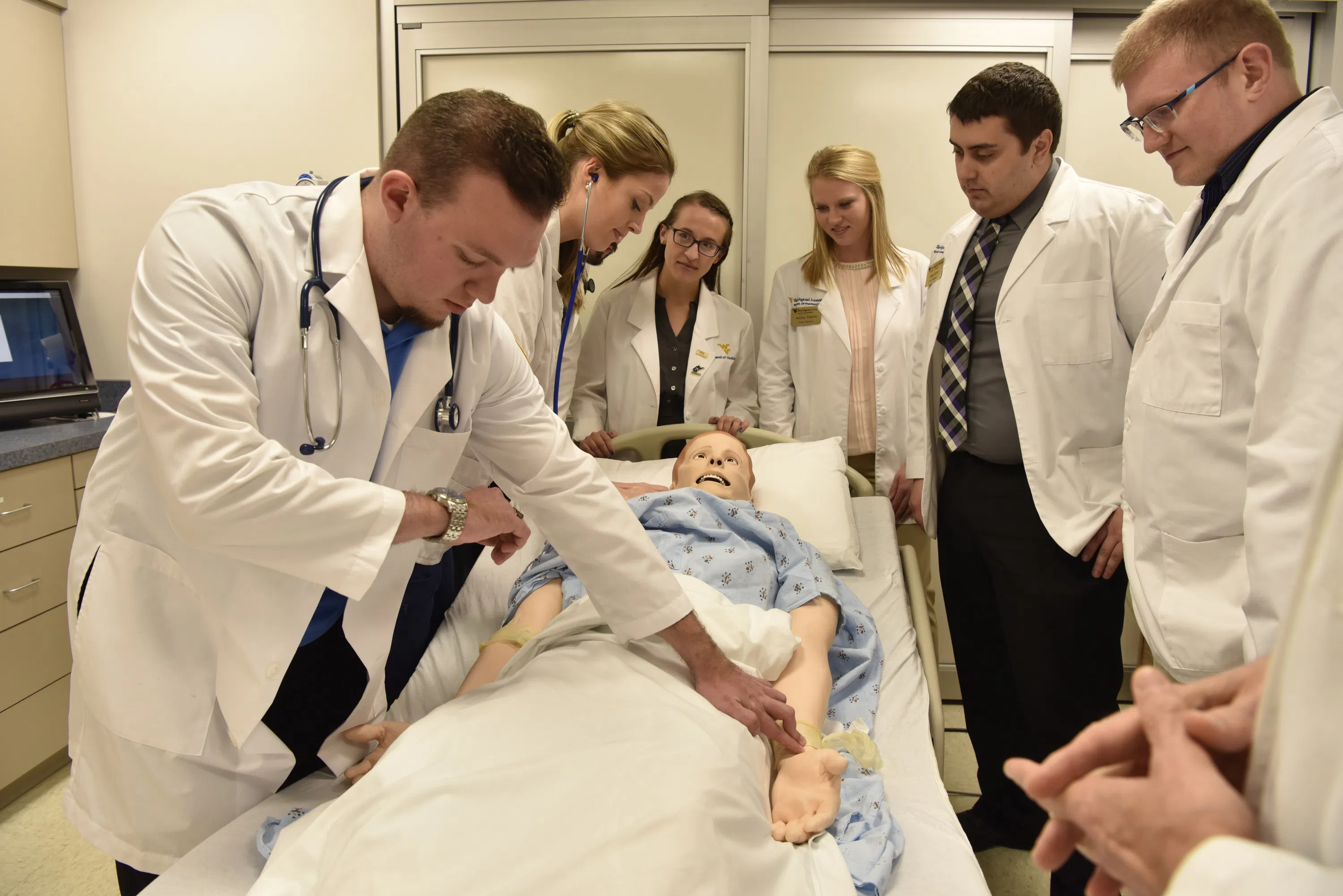 A group of Medical School Students gather around a training mannequin. 
