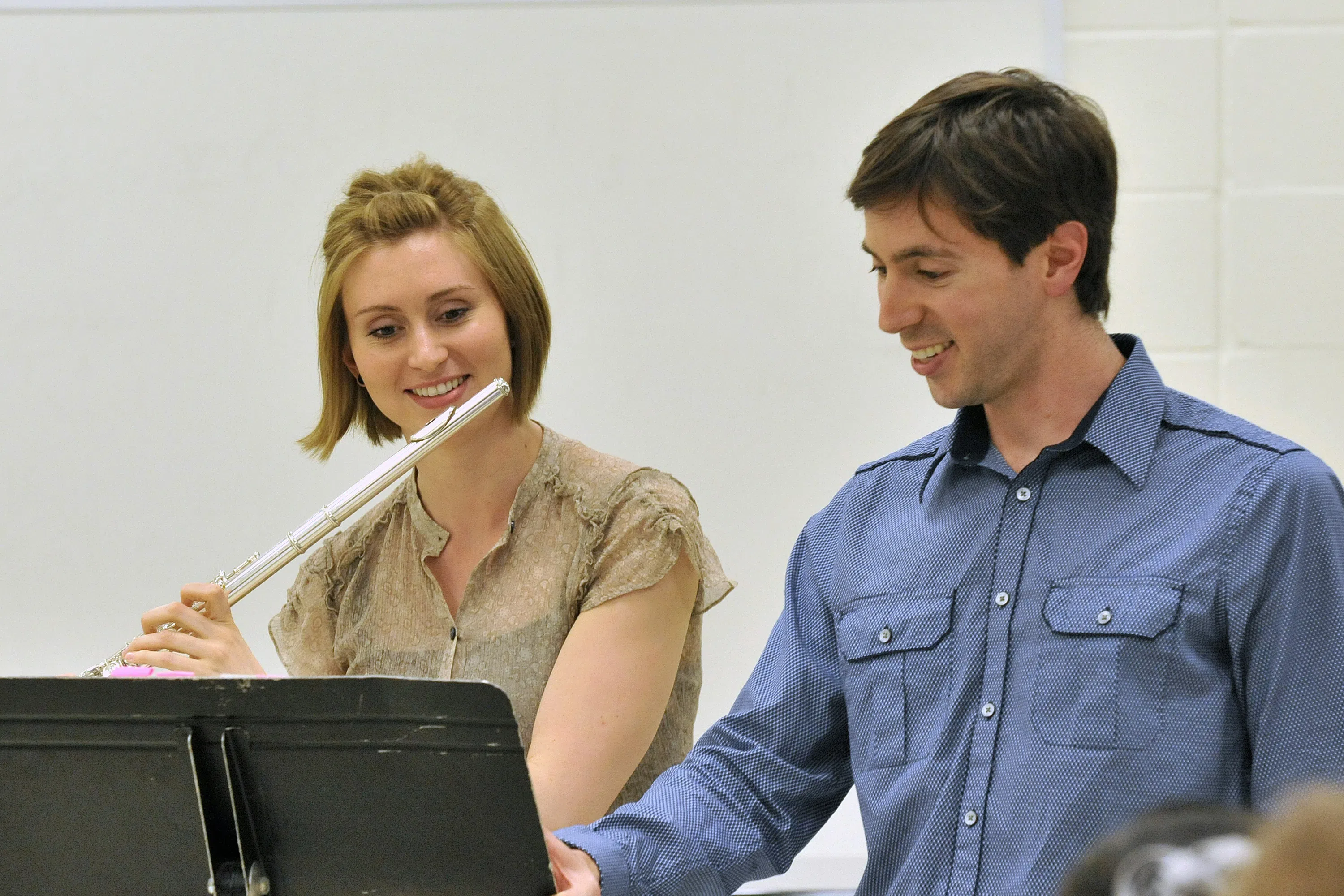 A photo of a student playing the flute as a faculty member instructs them.