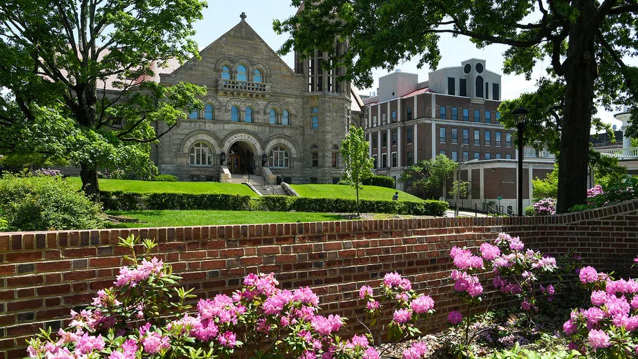 Stewart Hall pictured in the distance behind pink flowers on a sunny spring day.