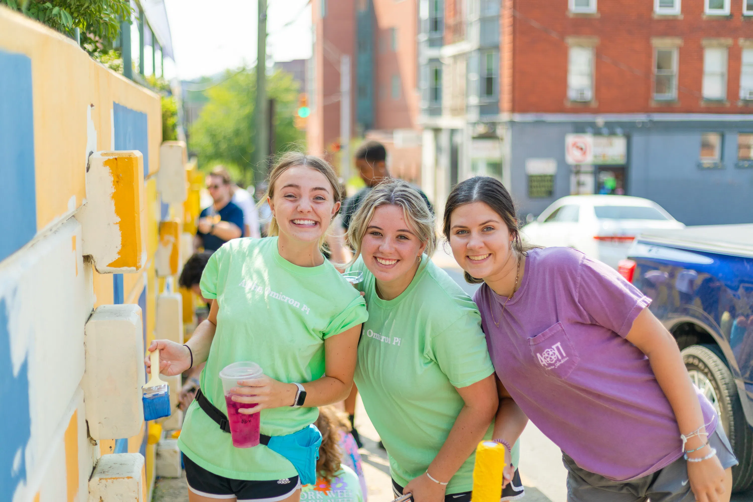 Three members of a sorority pose with painting equipment.