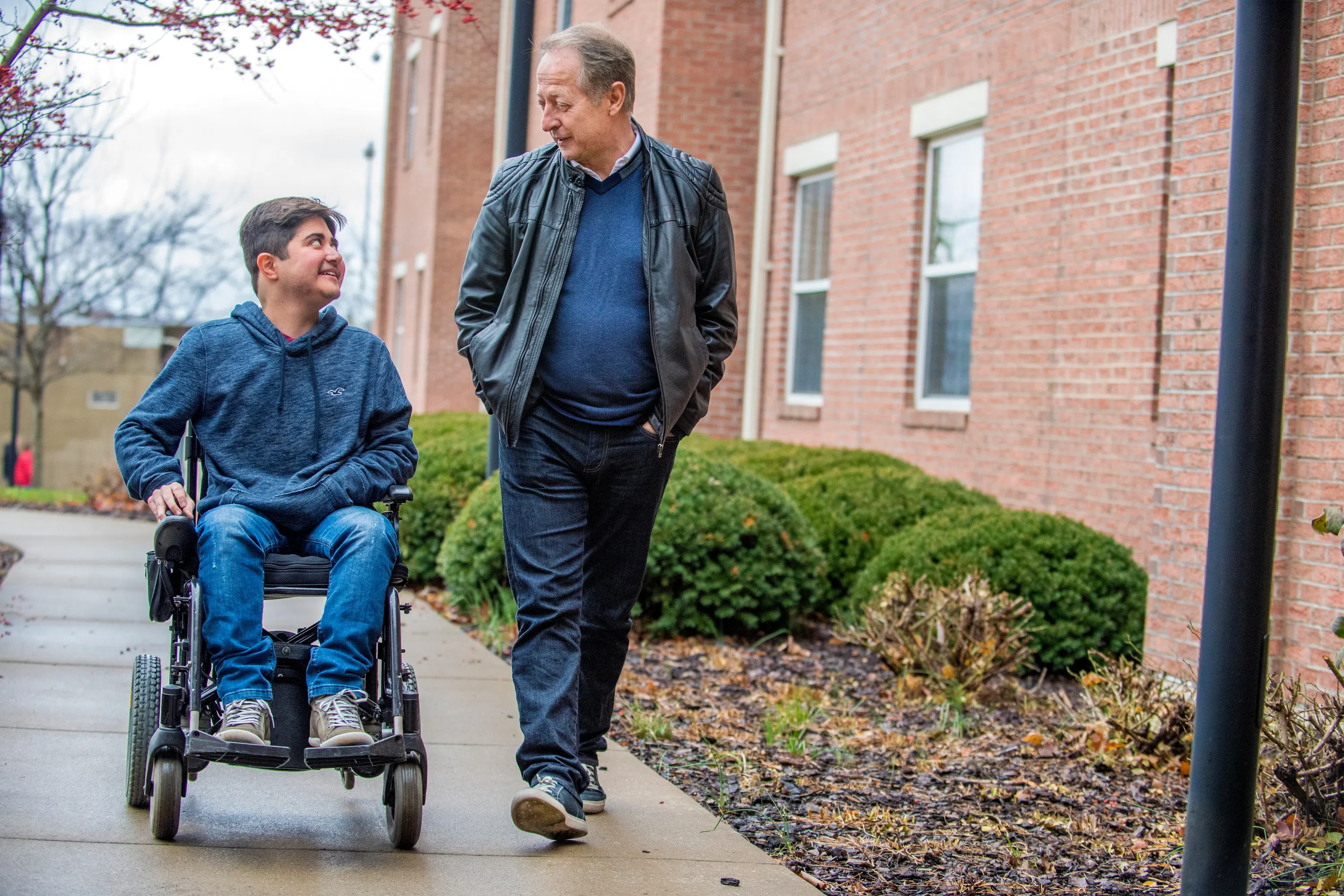A student in a wheelchair and a man pictured on the sidewalk.