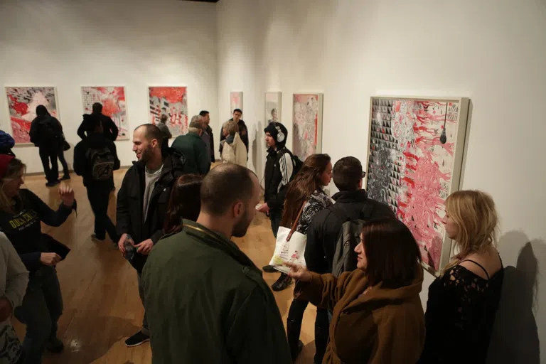 A large group of people stand in the art museum talking and viewing art.