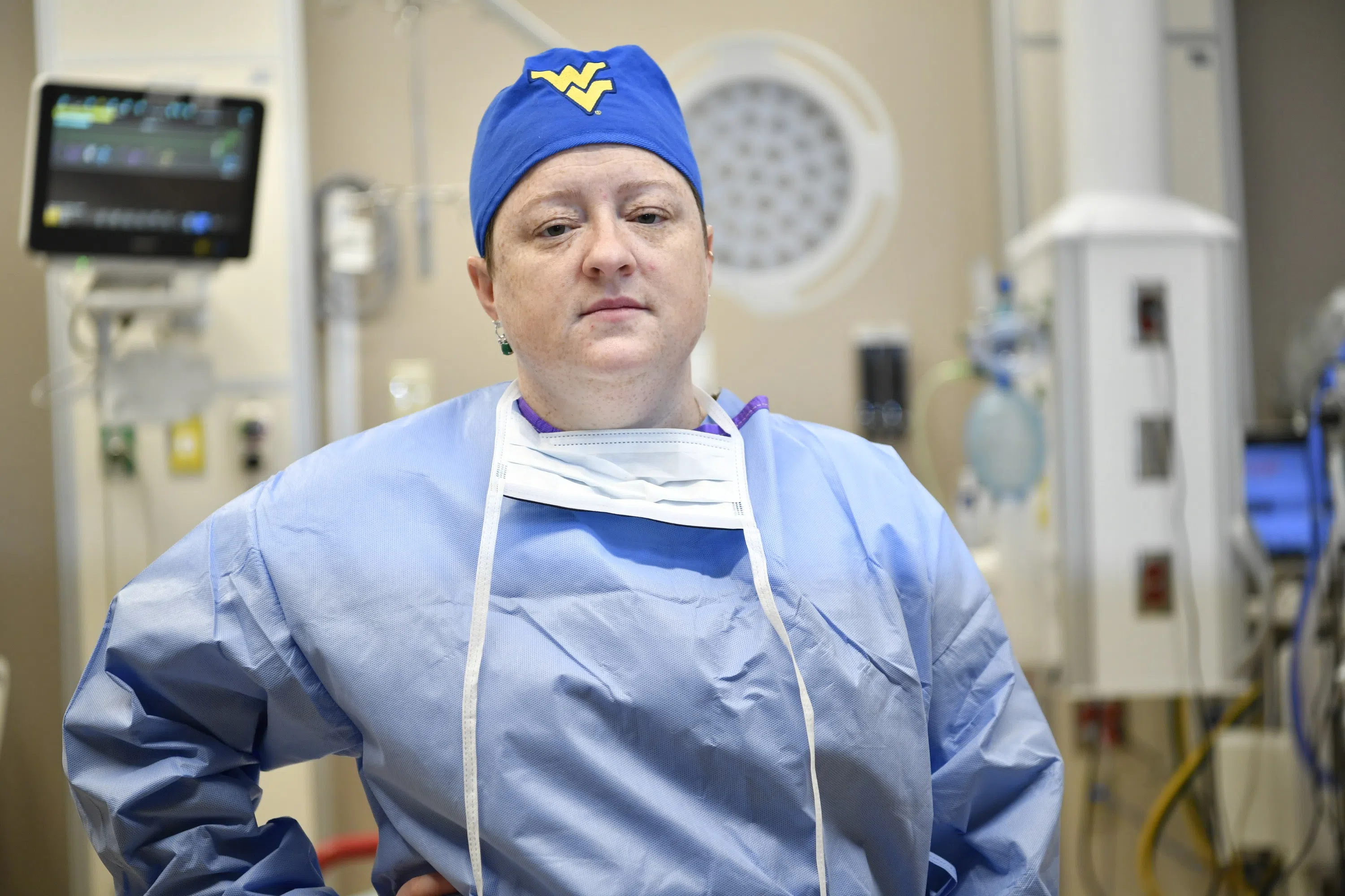 A nurse in scrubs and a flying WV headband looks into the camera.