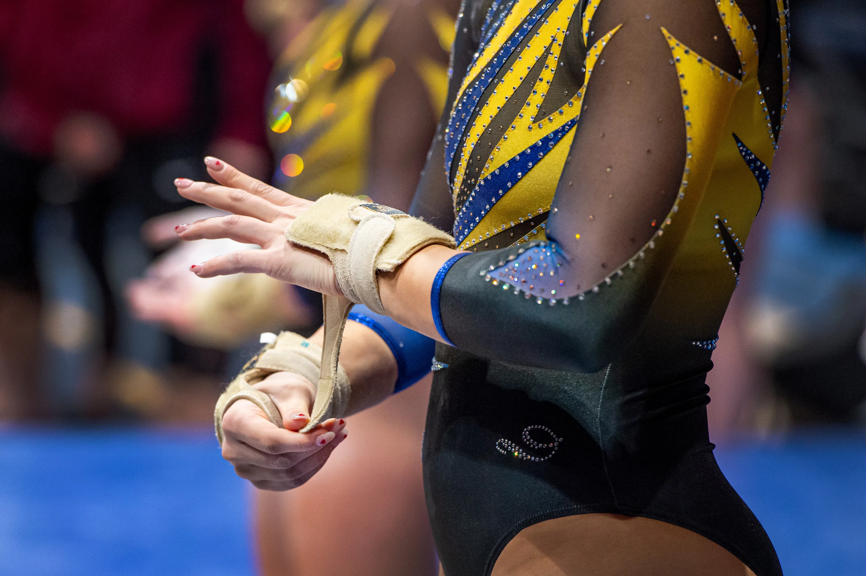 A gymnast adjusts the straps on her hand grips.