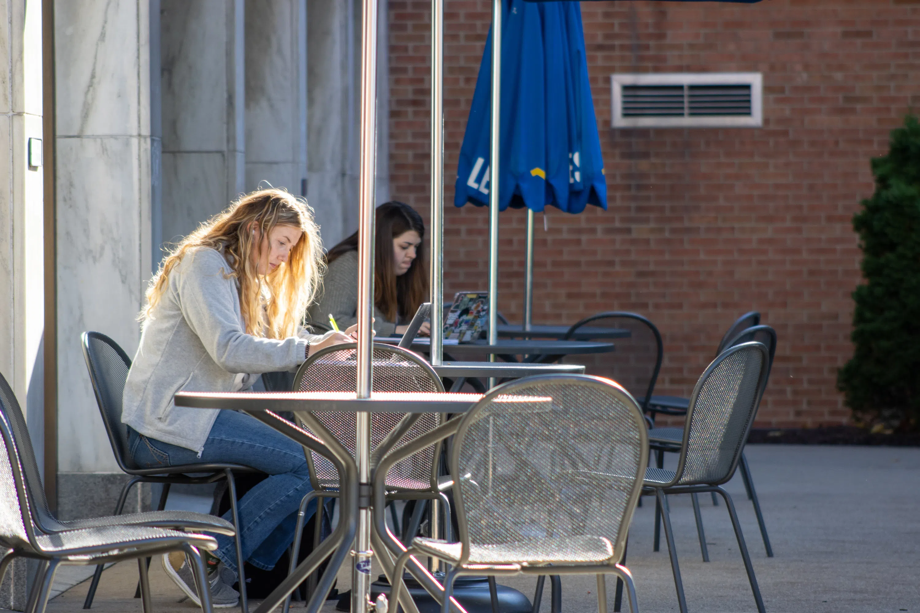 A student sits at the tables outside the Bookstore with their laptop. 