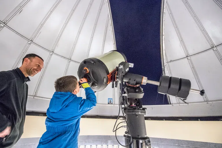 Young boy looks through the telescope at the observatory.