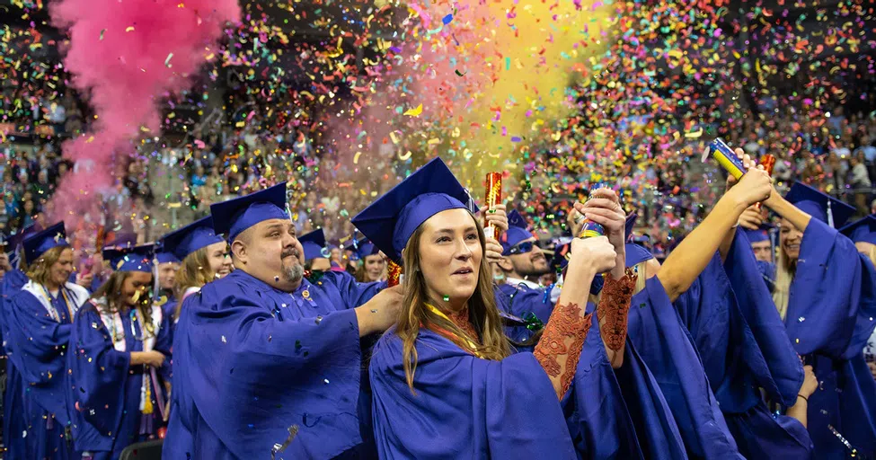 New graduates celebrate in cap and gown with confetti and colorful poppers