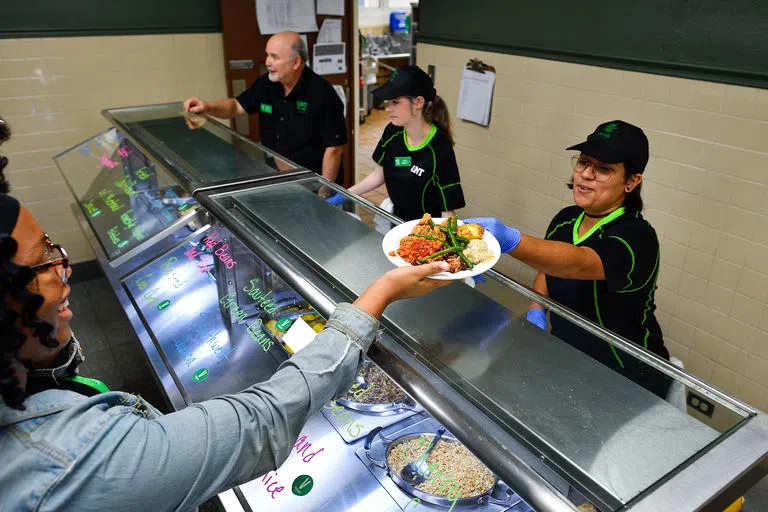 A Dining employee hands a student a plate of food.