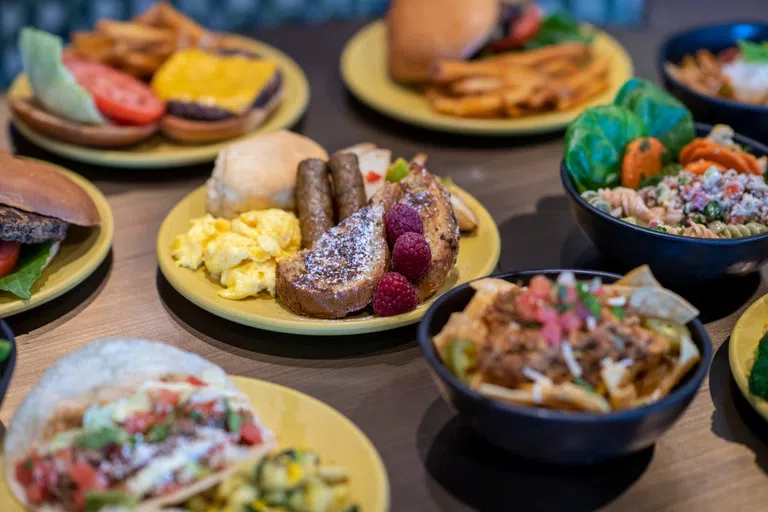 Close up of a breakfast plate holding french toast, eggs, sausage and a biscuit. Other plates of food surround the breakfast plate and are blurred in the image. 