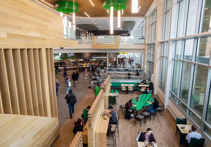 Aerial shot of the interior of Eagle Landing. People sit at tables, eating food, while others mill about the space to get food from one of the different stalls. 