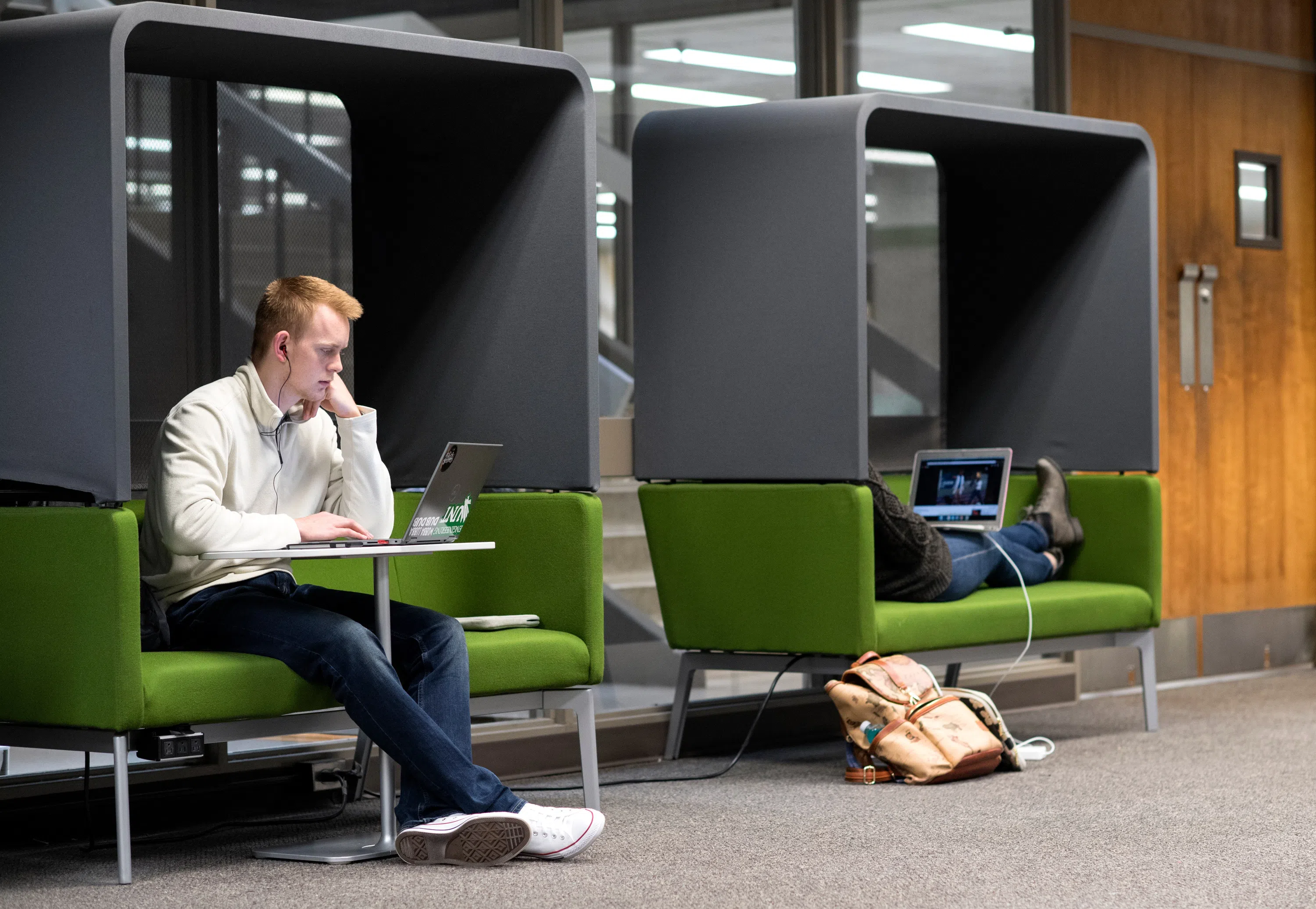 Two students sit in individual study pods with their computers