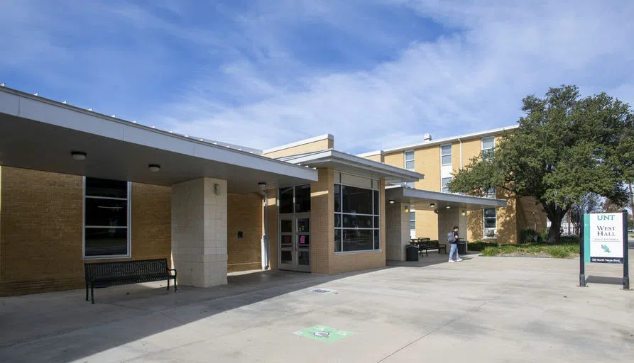 A photo of the exterior of West Hall on a sunny day with a student walking to class. 