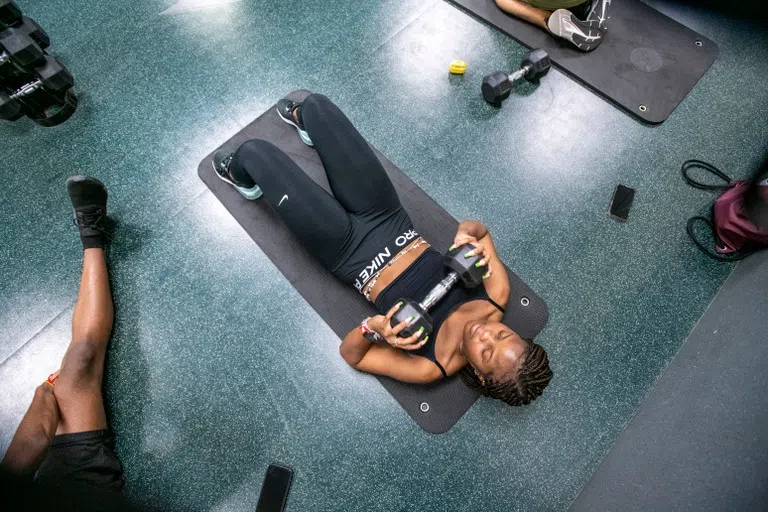 Student lays on a mat and utilizes a free weight