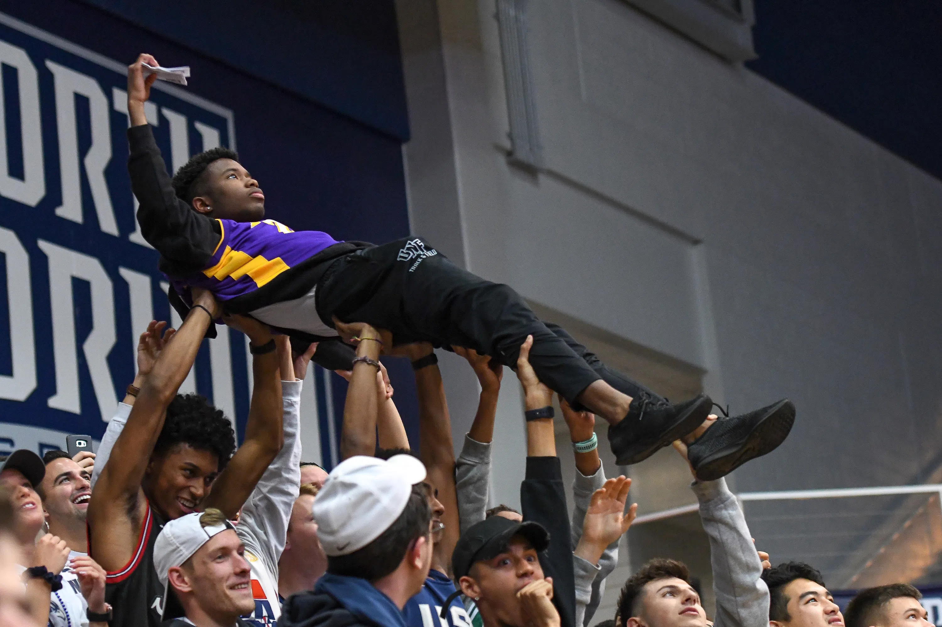 Students holding a student above their heads in the stands at a basketball game