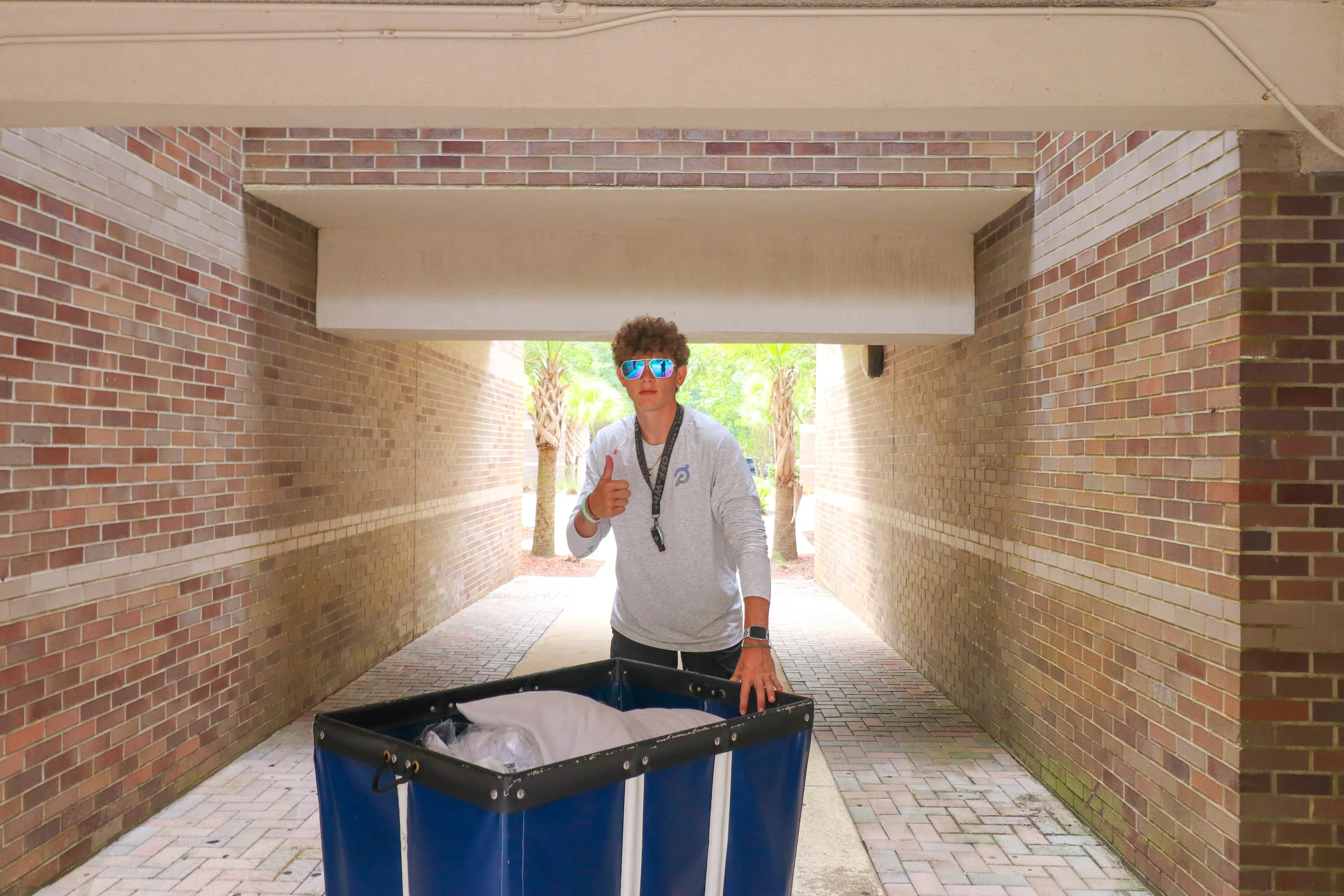 Student pushing move-in cart and giving a thumbs up in Osprey Landing atrium entrance