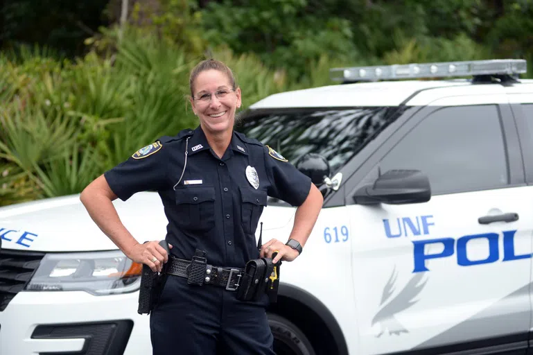 Police Officer poses in front of UNF police car