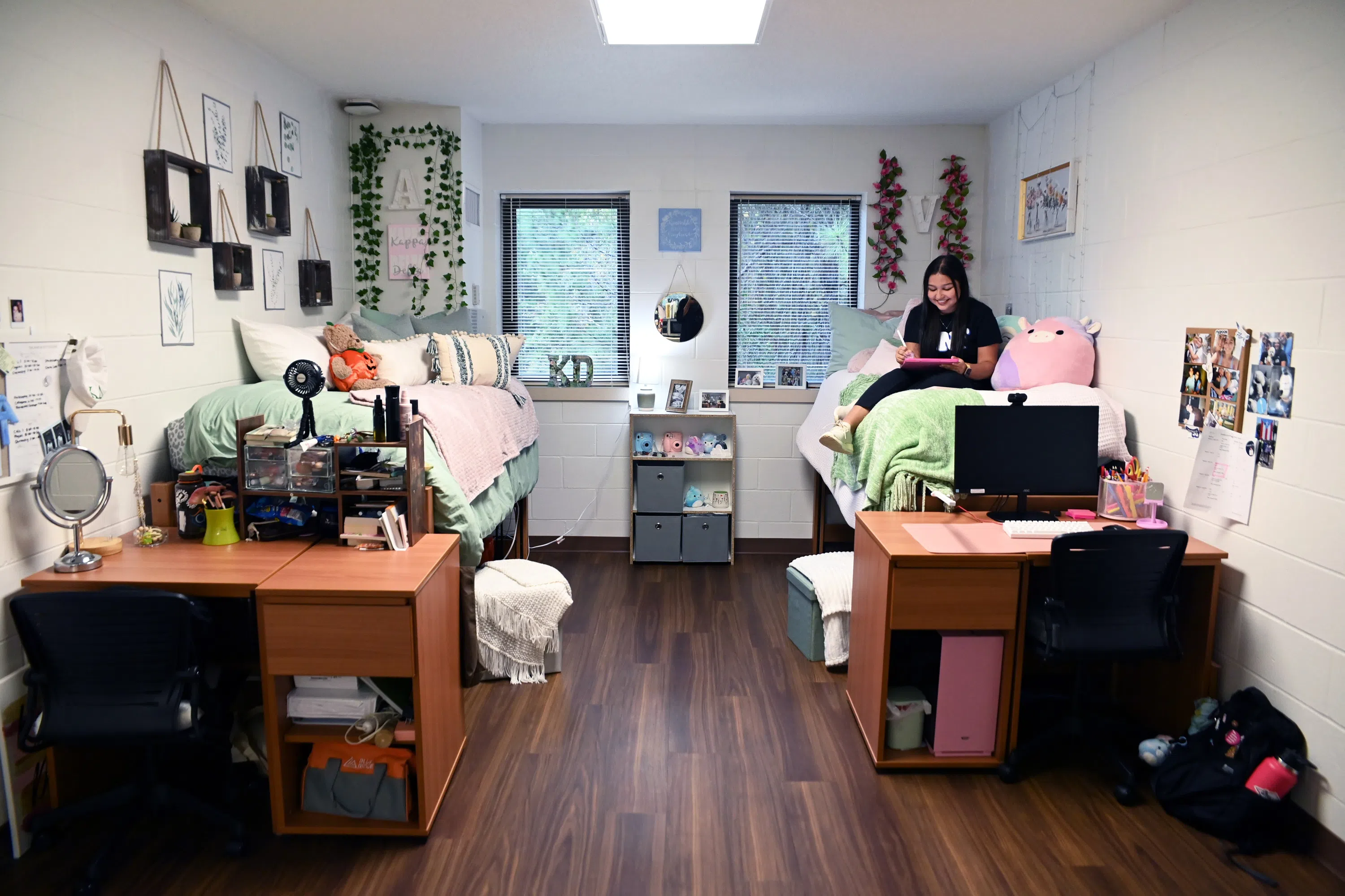 Student sits on bed in decorated residential room with two beds and two desks