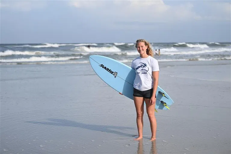 UNF Surf Club student standing with surfboard on the beach