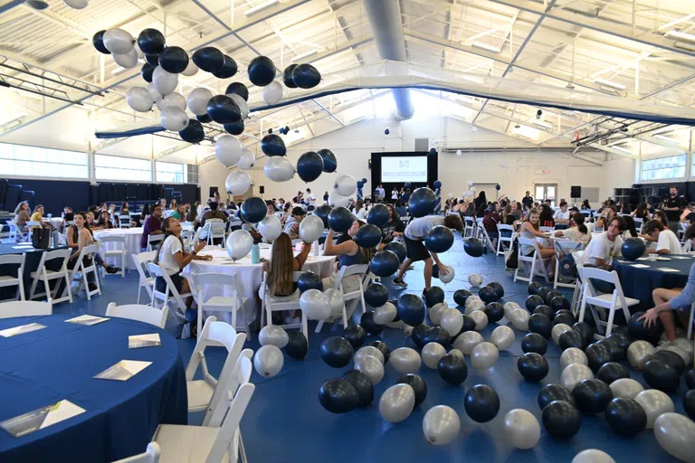 Balloons floating down over students seated at tables in the Field House