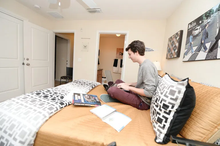 Student sitting on bed working on computer in Flats room