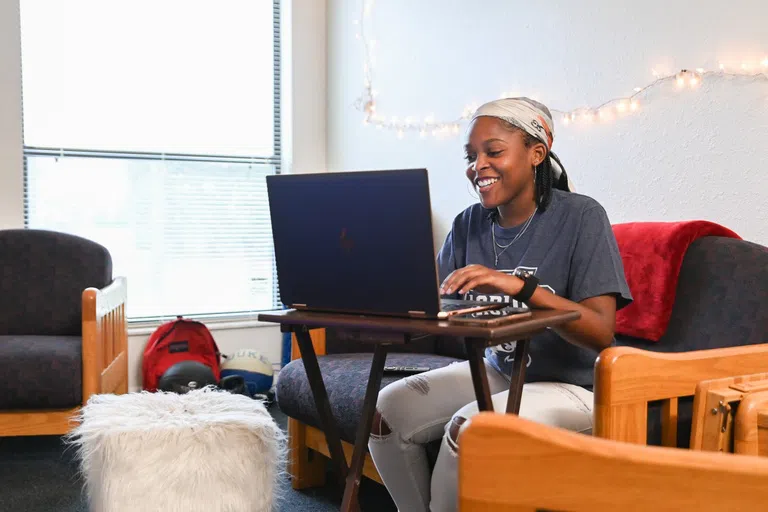 Student sitting on couch, working on computer on a side table 