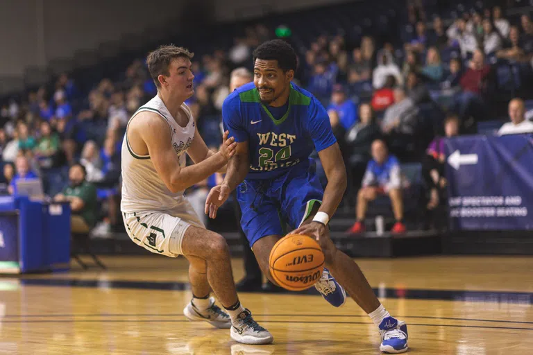 Men's basketball player dribbling around a defender.