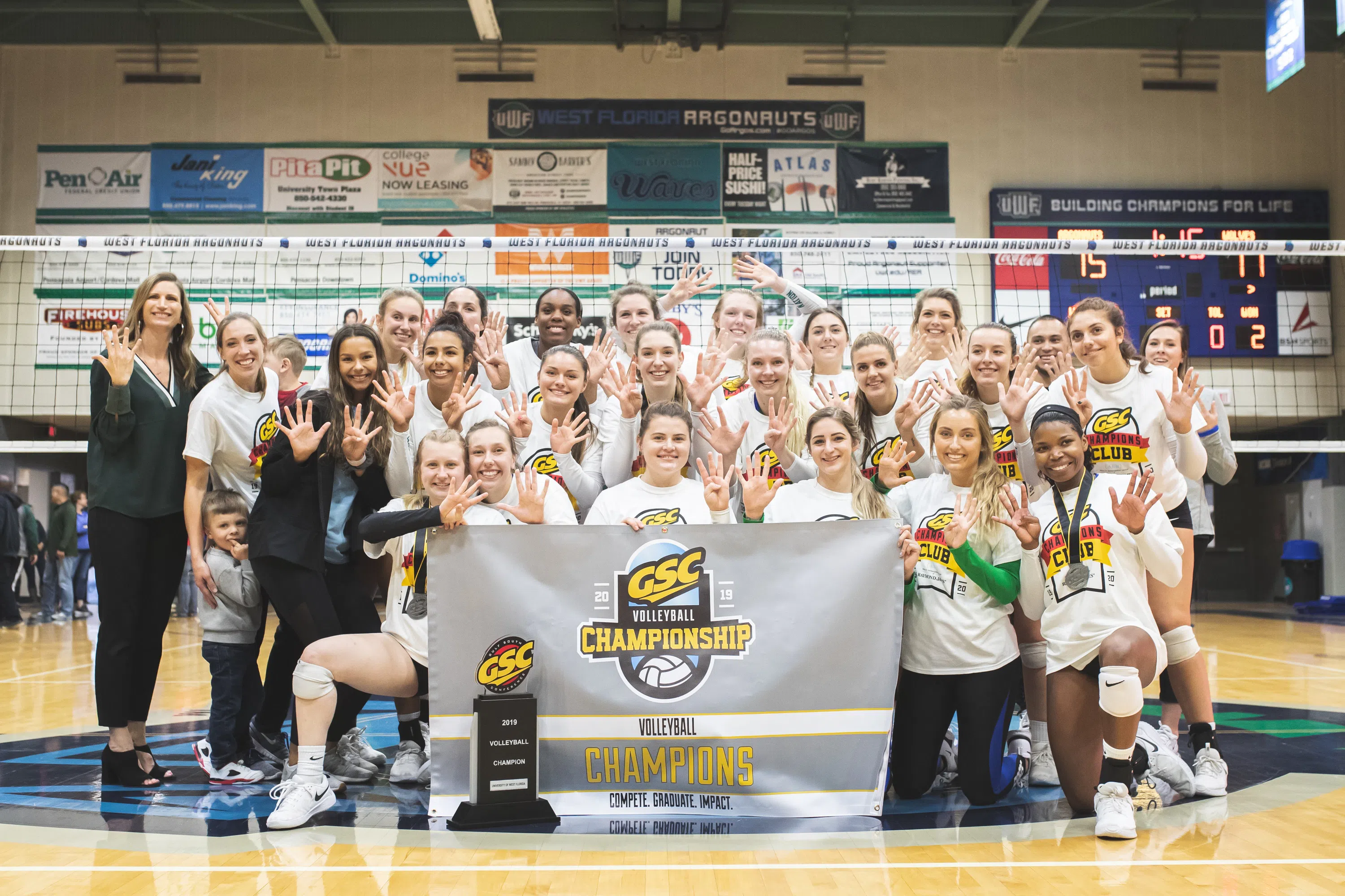 Women's volleyball team poses on the court with championship trophy