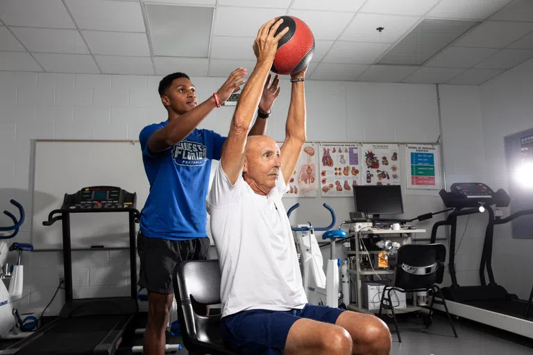 Student works with a gentleman's range of motion and strength with a large ball.