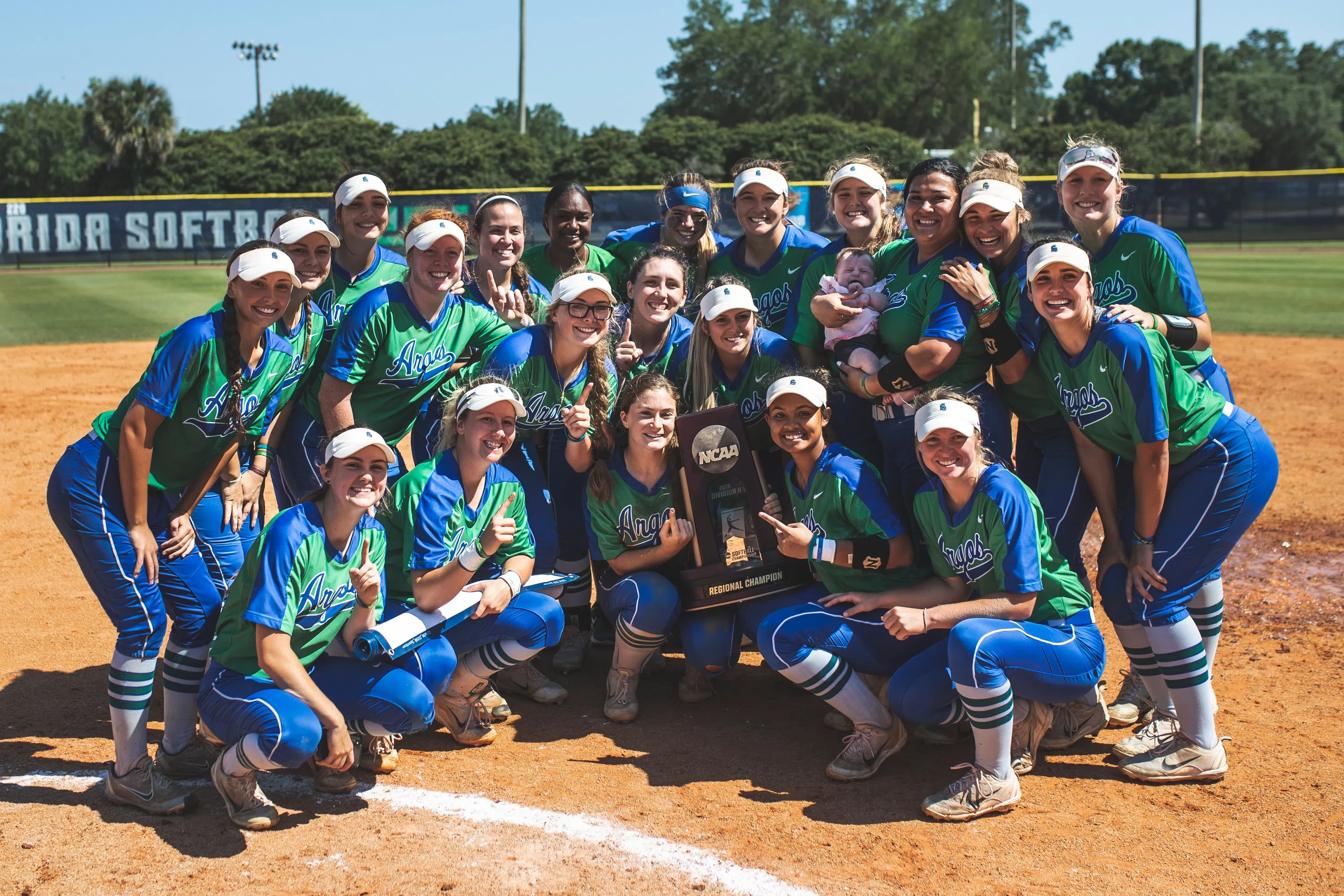 Softball team poses on field with championship trophy.