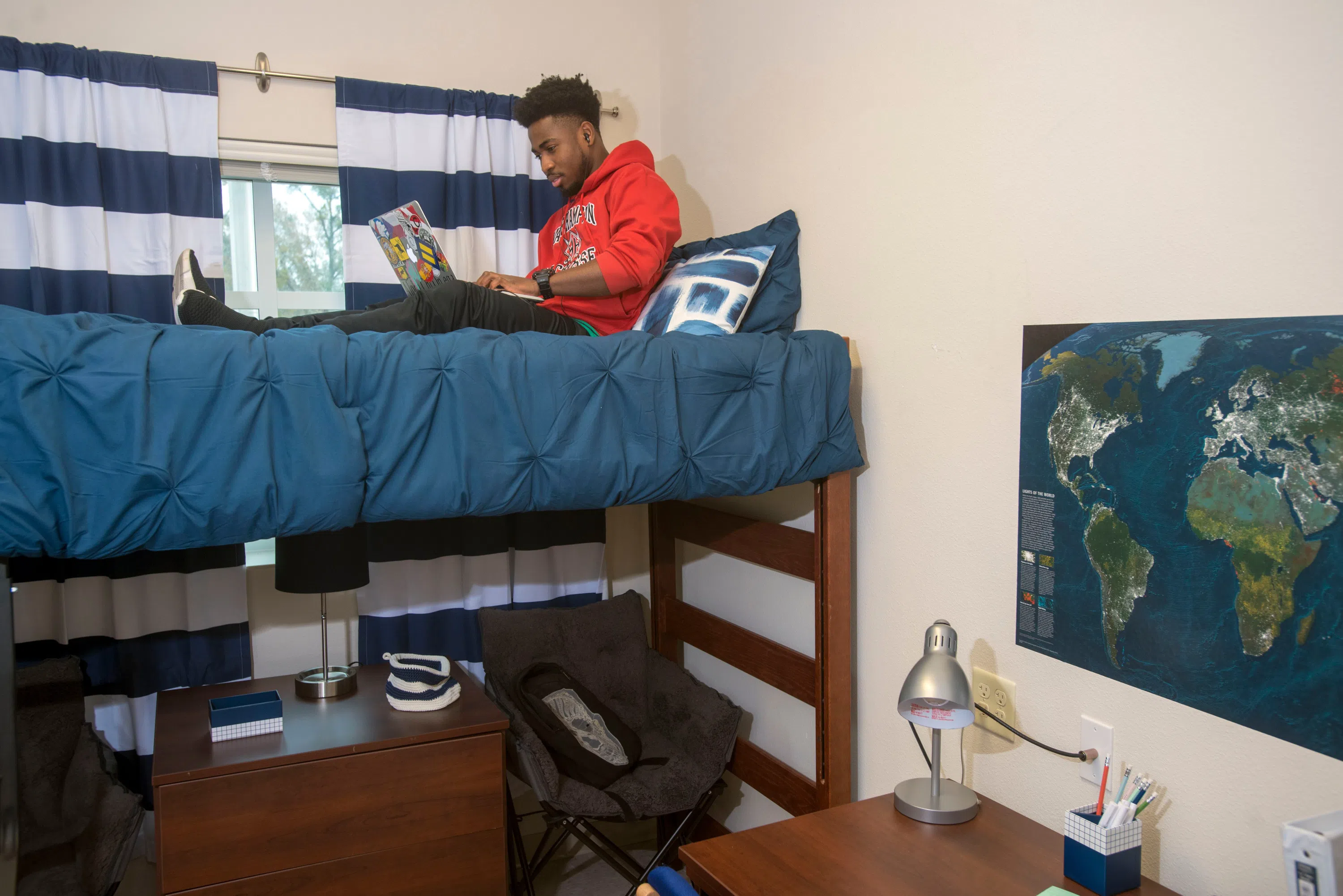 A male student on laptop on his lofted bed in Presidents Hall