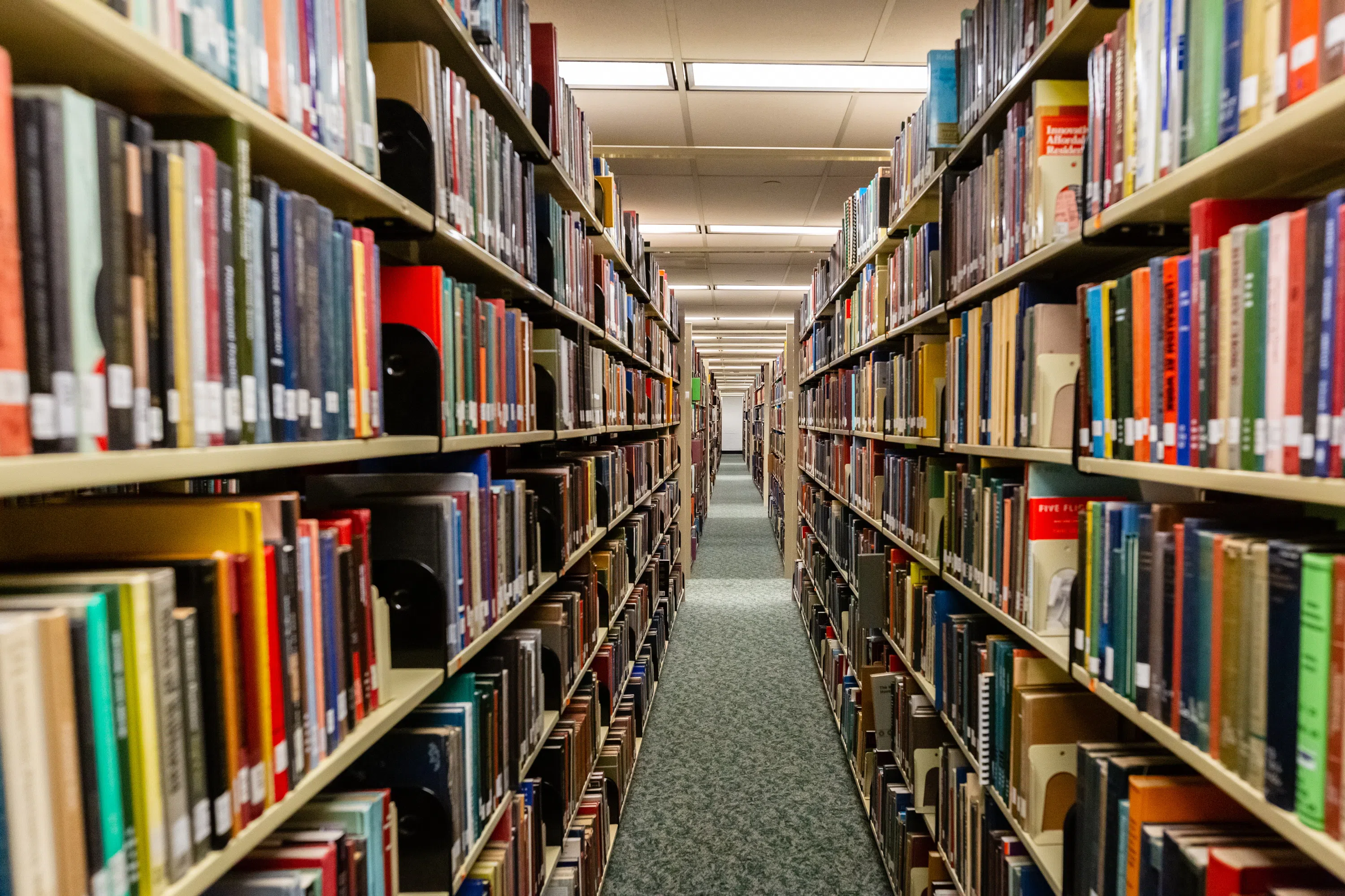 Filled book shelves on each side, creating an aisle to walk through with a green carpet.