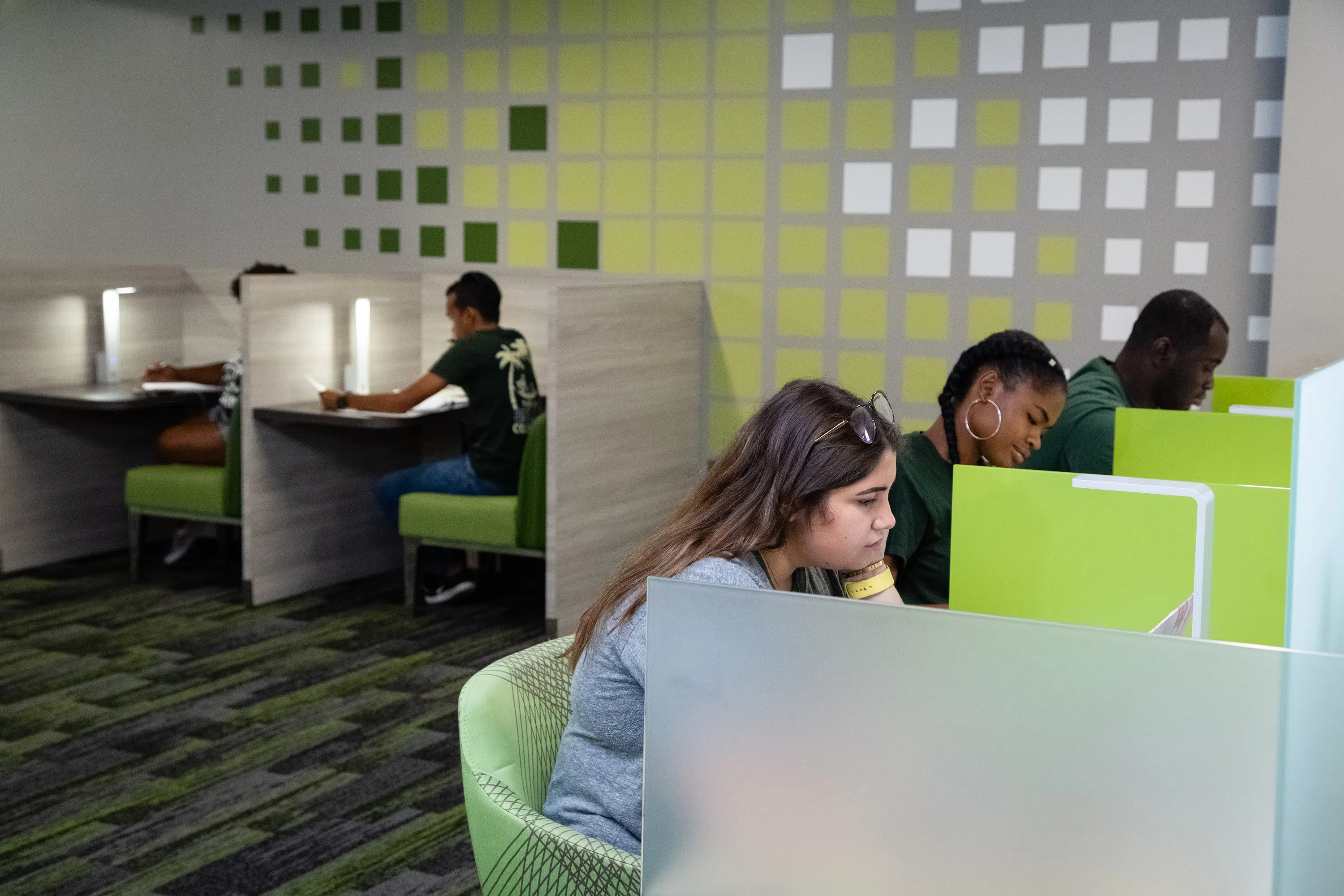 Students studying at the Library in personal seating arrangements. Plastic dividers attached to the desks divide the seats up.