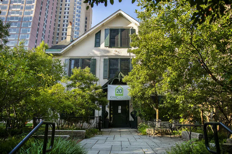 A white, 3-story 1850s house with dark green shutters framed by large trees, with a "20 Years: Civic House" banner in front.