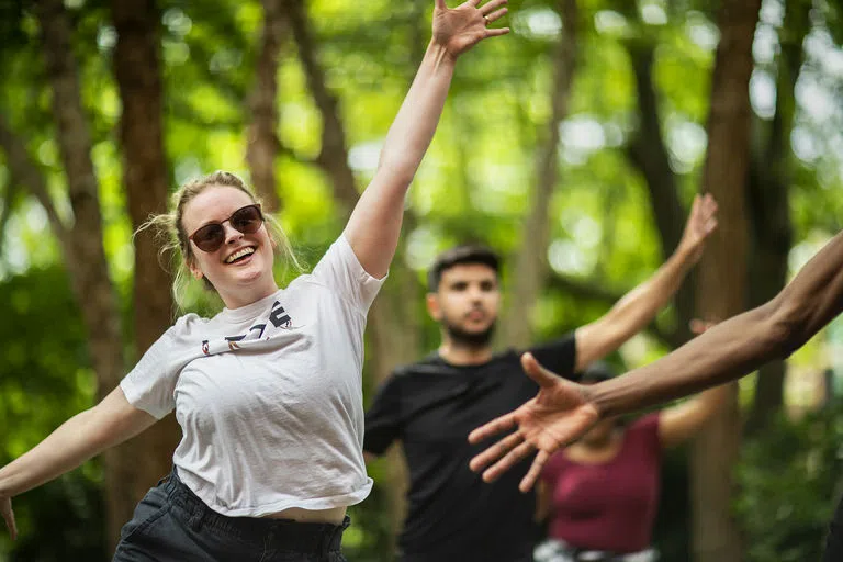 Students are smiling and engaged in a dance class with their arms outstretched.