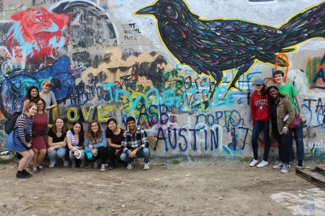 A dozen students pose together in front of a vibrant graffiti wall, with "ASB (Alternative Spring Break): Austin 2017" written on it.