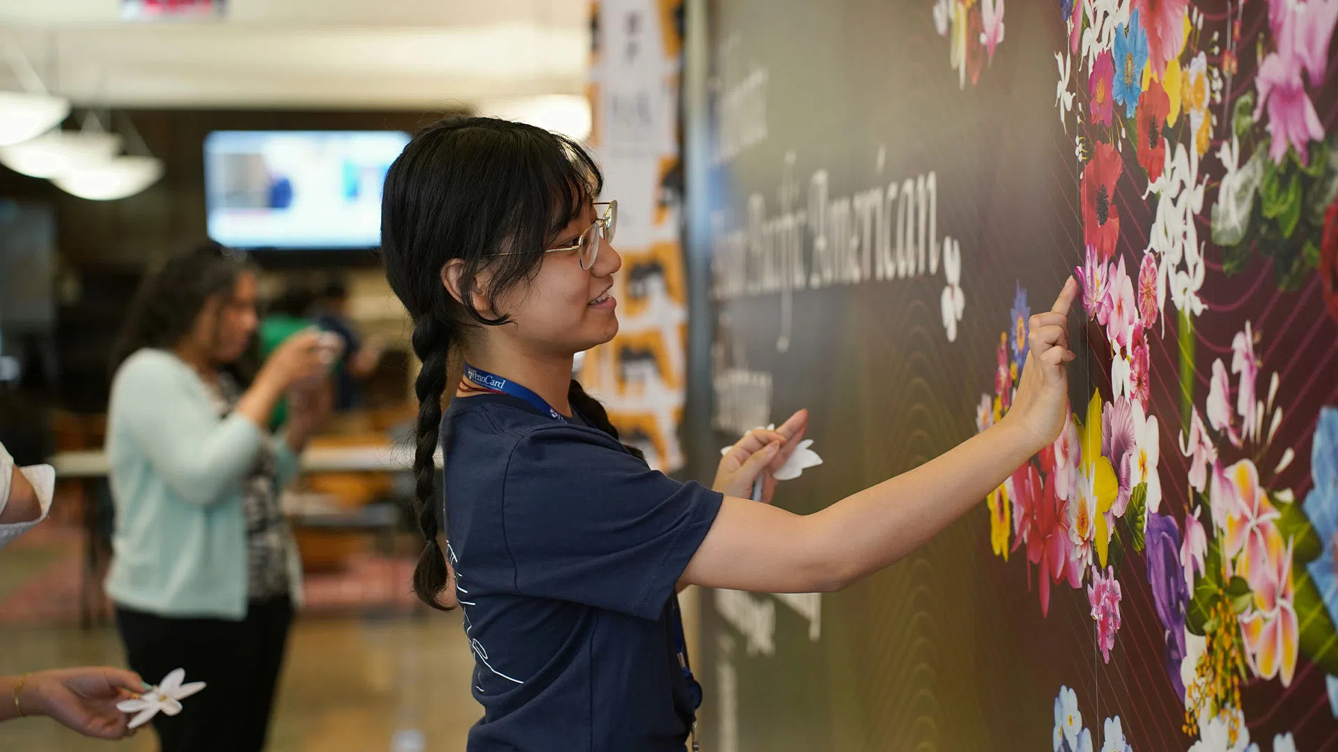 Student decorating mural with a sticker of a flower. Each flower represents a different Asian-Pacific cultural identity. 