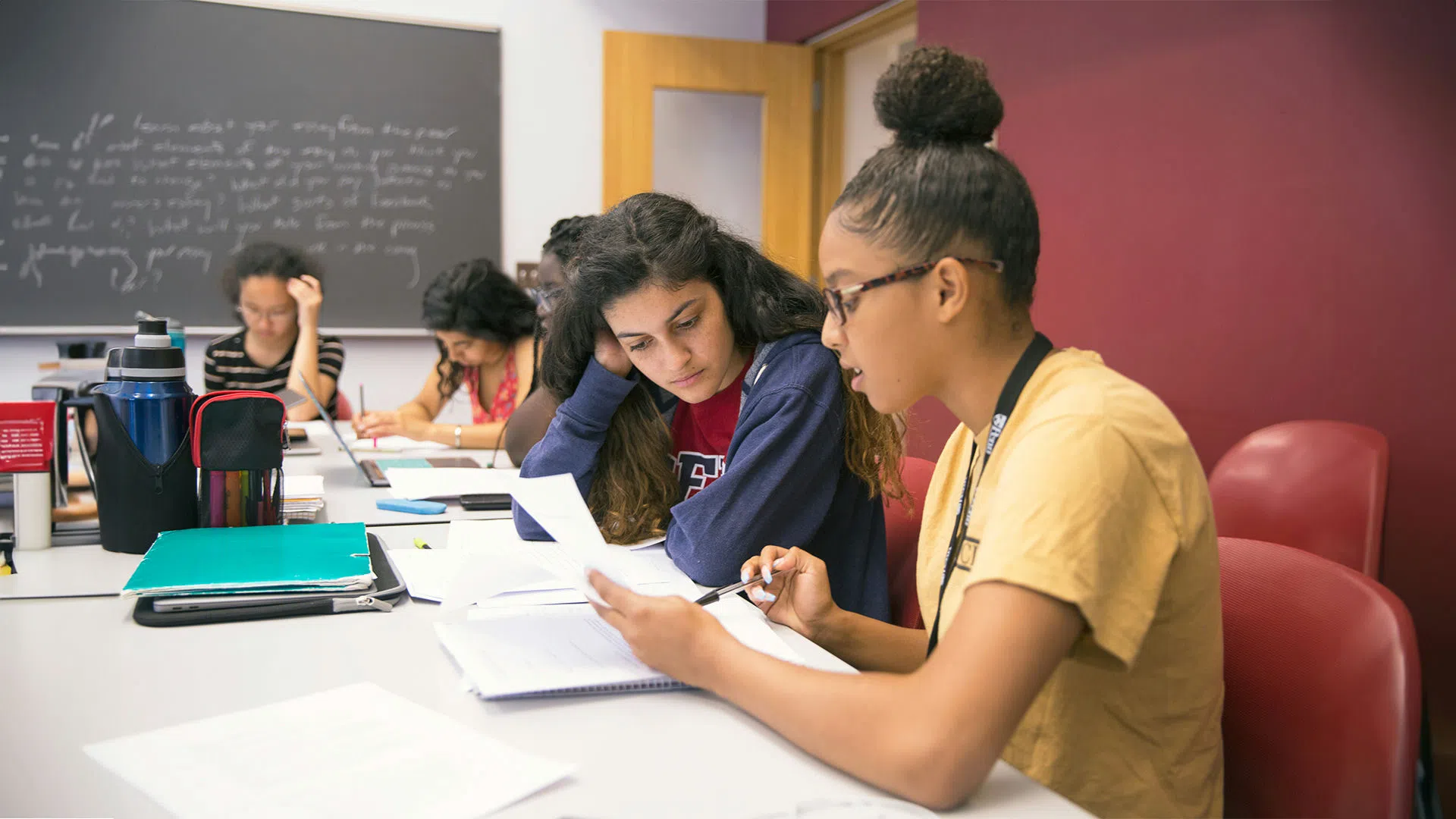 A student attentively listens to a peer during group tutoring in a classroom setting, receiving instructional support.